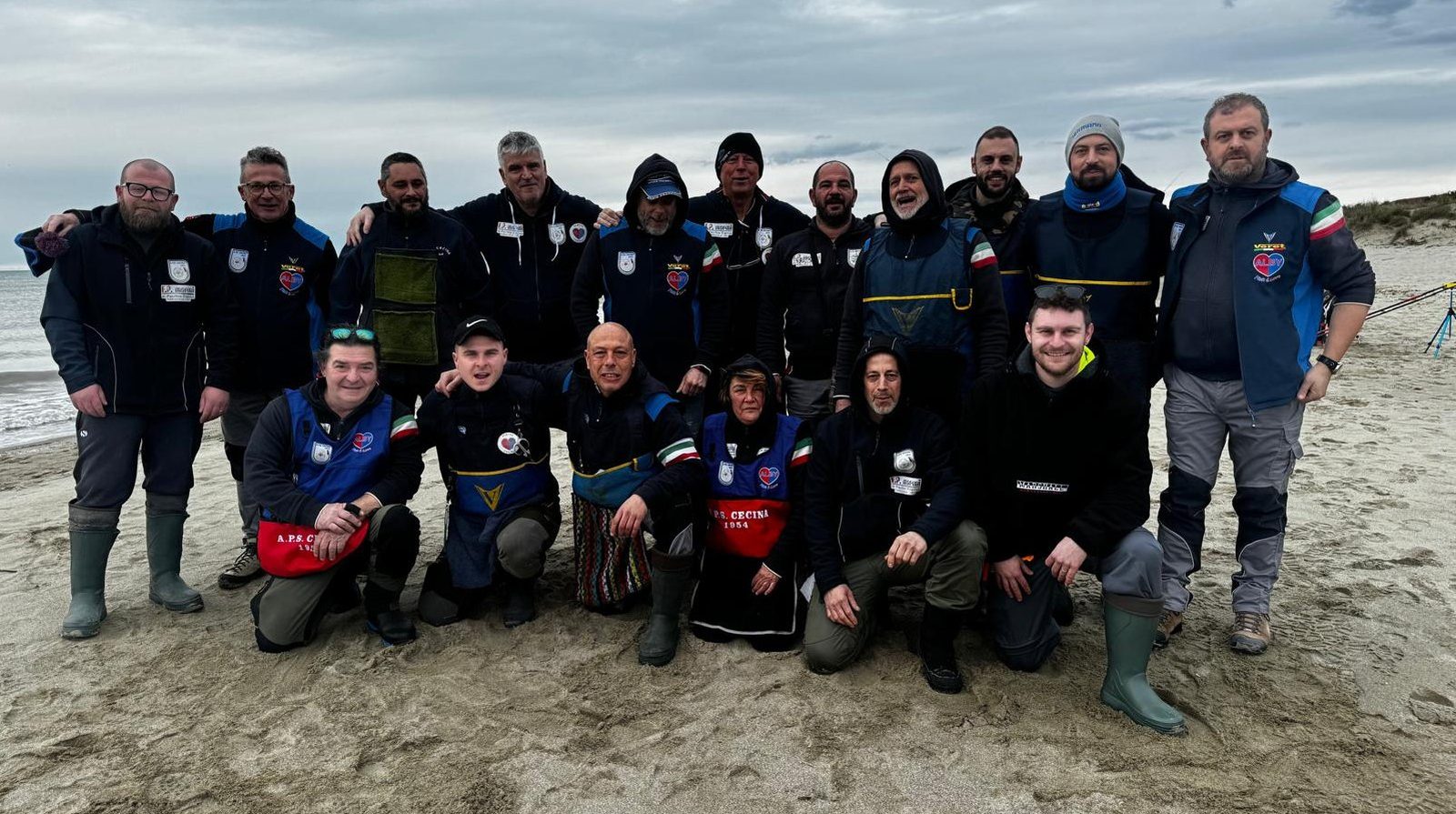 La squadra dell'APS Cecina in spiaggia, con le giacche blu e le pettorine rosse della società